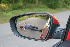 Concept of a hit and run: Injured man lying on the road, seen through the rearview mirror of a car.